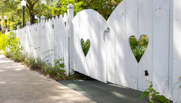 A white wooden fence around a home with heart shapes cut out.